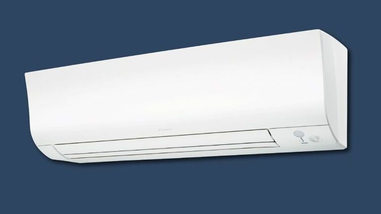 Veggmontert klimaanlegg med synlig luftspjeld og knapp for manuell betjening.